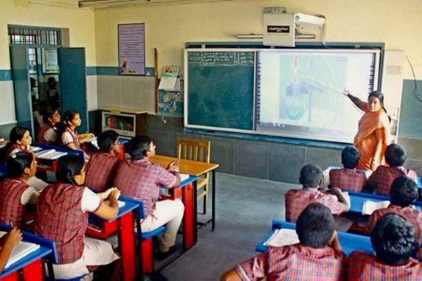 A teacher taking class in a smart board to a group of students in the classroom
