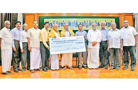 12 men are seen standing on the stage and one of them is handing over a big cheque leaf to another person